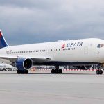 Delta Airlines airplane on airport runway, cloudy sky.