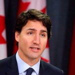 Man speaking in front of Canadian flags.