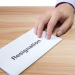 Hand holding a resignation letter on table.