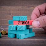 Hand holding red block labeled ethics above blue blocks.