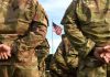 Soldiers stand in formation with American flag in background
