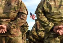 Soldiers stand in formation with American flag in background
