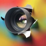 Camera lens poking through torn colorful background