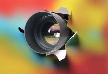 Camera lens poking through torn colorful background