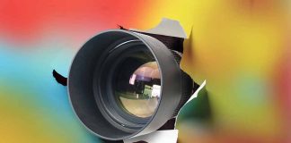 Camera lens poking through torn colorful background