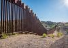 Tall metal border fence in desert landscape sunlight