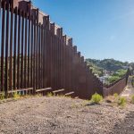 Tall metal border fence in desert landscape sunlight