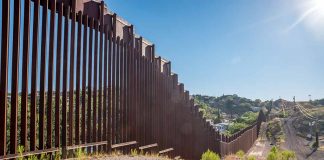 Tall metal border fence in desert landscape sunlight