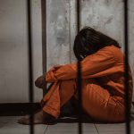 Person in orange jumpsuit sitting behind bars head down