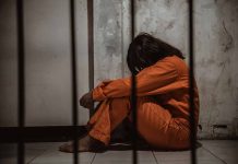Person in orange jumpsuit sitting behind bars head down
