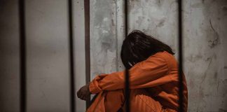 Person in orange jumpsuit sitting behind bars head down