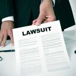 Person holding a document titled LAWSUIT in office