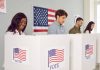 People voting in booths with American flag backdrop