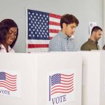 People voting in booths with American flag backdrop