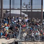 Crowd of people sitting near border fence outdoors