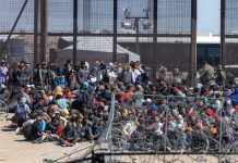 Crowd of people sitting near border fence outdoors