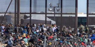 Crowd of people sitting near border fence outdoors