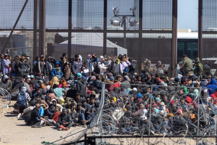 2497167493 featured image Crowd of people sitting near border fence outdoors