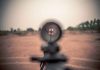 Rifle scope aimed at a distant target outdoors