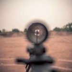 Rifle scope aimed at a distant target outdoors