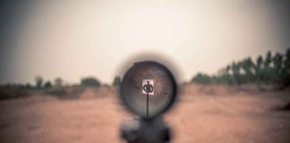 Rifle scope aimed at a distant target outdoors