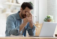 Man rubbing eyes holding glasses near laptop