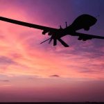 Silhouette of a drone against a colorful sunset.