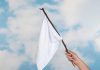 Hand holding white flag against a blue sky.