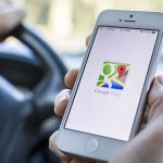 A person holding a smartphone displaying the Google Maps app while driving