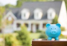 A blue piggy bank in front of a blurred house and greenery