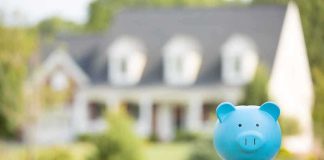 A blue piggy bank in front of a blurred house and greenery