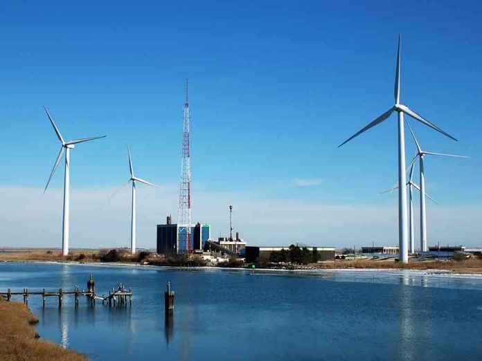shutterstock_2718216.jpg Wind turbines and a communication tower near a body of water under a clear blue sky