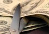 Scissors cutting through a stack of dollar bills