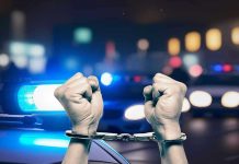 Handcuffed hands raised police cars with lights on