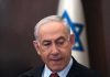 Man in suit with Israeli flag in background.