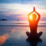 Person meditating on the beach during sunset