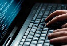 Close-up of hands typing on a laptop keyboard with code displayed on the screen