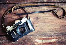A vintage camera resting on a wooden surface with a leather strap