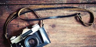 A vintage camera resting on a wooden surface with a leather strap