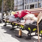 Person sleeping on park bench with cardboard sign.