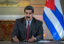Man speaking at podium with Cuban flag in background.