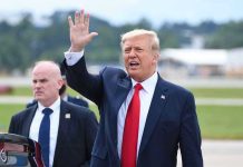Man in suit waving while another man stands nearby.