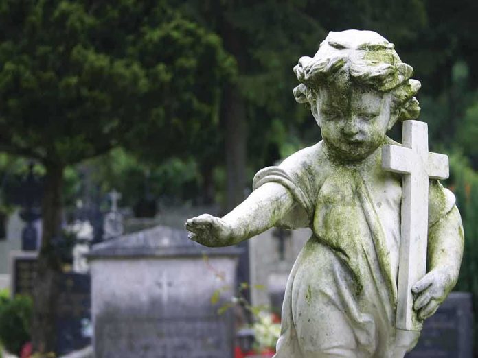 shutterstock_156593303.jpg Weathered statue of a child angel holding a cross in a cemetery