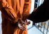 Shocking Prison Blunder – Convicted Offender Freed! Handcuffed person in orange jumpsuit being escorted.