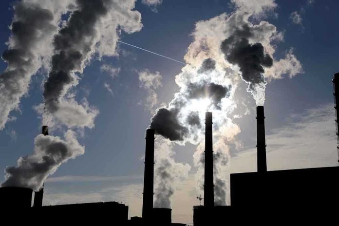 shutterstock_226073734.jpg Silhouetted smokestacks emitting smoke against a cloudy sky with sunlight