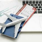 A model airplane on a blue passport next to a laptop and boarding pass