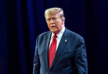 Trump Whispers Two-Word Insult – Shocks Media Man in suit with red tie speaking on stage.