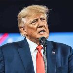 Trump Targeted: Mamdani Fires WARNING SHOT! Man in suit speaking at a microphone.