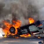 Car EXPLODES – Erupts into Blazing Inferno An overturned car engulfed in flames and smoke on a city street