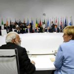 People seated around a large round table, flags behind.